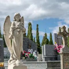 Anioł stróż na cmentarzu, symbol spokoju i pamięci. W tle wysokie cyprysy i nagrobki, tworzące melancholijną atmosferę.