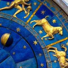 Złote figury Koziorożca i innych znaków zodiaku na niebieskiej tarczy zegara. 19 stycznia to czas Koziorożca.