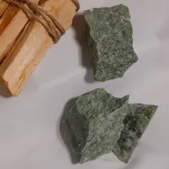 Surowe kawałki zielonego jadeitu, kamienia o cenionych właściwościach, leżą obok wiązki drewna Palo Santo.