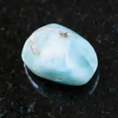 Gładki, błękitny kamień larimar, znany ze swoich uspokajających właściwości, leży na ciemnym, błyszczącym tle.
