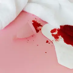 Sennik krew menstruacyjna: kubeczek i podpaska z plamami krwi na różowym tle.