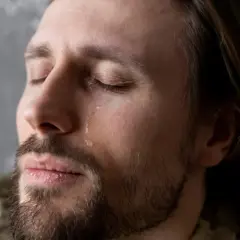 Mężczyzna z zamkniętymi oczami, po policzku spływa łza. Sennik płacz sugeruje uwolnienie emocji.