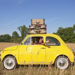 Radosna kobieta w żółtym samochodzie z bagażami na dachu, wyrusza w podróż. Sennik jazda samochodem zapowiada nowe przygody.