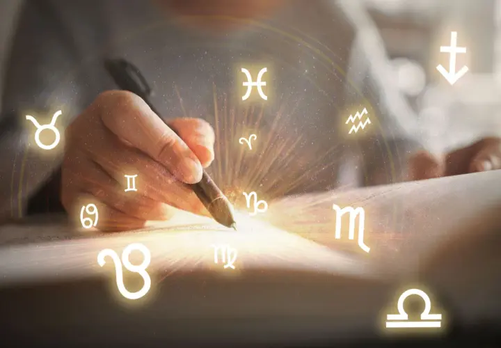 Dłoń pisze piórem, a wokół niej krążą wszystkie znaki zodiaku, tworząc magiczny krąg.