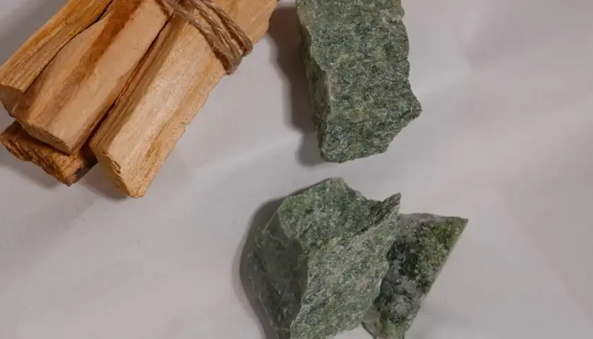 Surowe kawałki zielonego jadeitu, kamienia o cenionych właściwościach, leżą obok wiązki drewna Palo Santo.