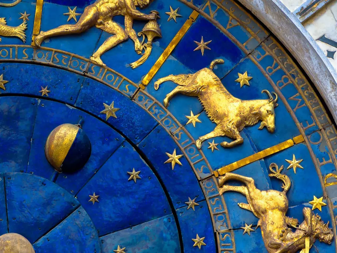 Złote figury Koziorożca i innych znaków zodiaku na niebieskiej tarczy zegara. 19 stycznia to czas Koziorożca.