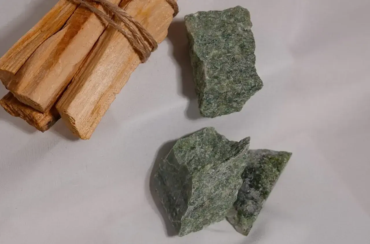 Surowe kawałki zielonego jadeitu, kamienia o cenionych właściwościach, leżą obok wiązki drewna Palo Santo.