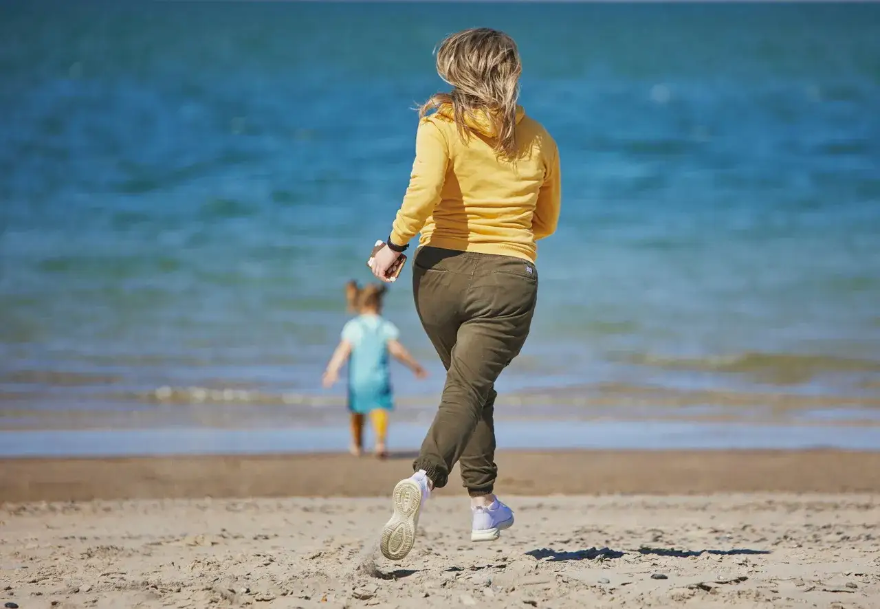 Kobieta biegnie na plaży do dziecka w wodzie. Sen o tym, by ratować kogoś z wody, może oznaczać potrzebę pomocy.