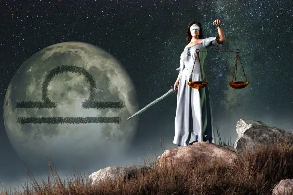 Kobieta z przepaską na oczach, trzymająca wagę i miecz, stoi na tle księżyca z symbolem Wagi. Ascendent w wadze.